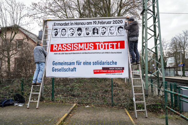 Aktion zum Jahrestag der raassistischen Morde von Hanau. Ein Banner wird an einer Plakatwand angebracht